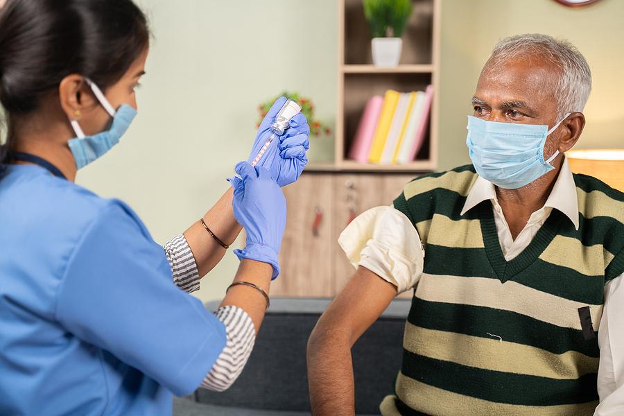 Doctor preparing vaccination shot to elderly patient by holding syringe at home - concept of home health check to seniors during coronavirus covid-19 pandemic.