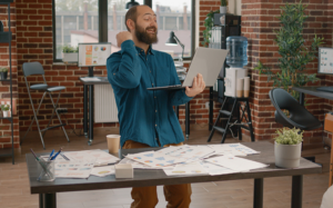 Happy Employee with raised fist holding laptop, charts and graphs spread out on desk